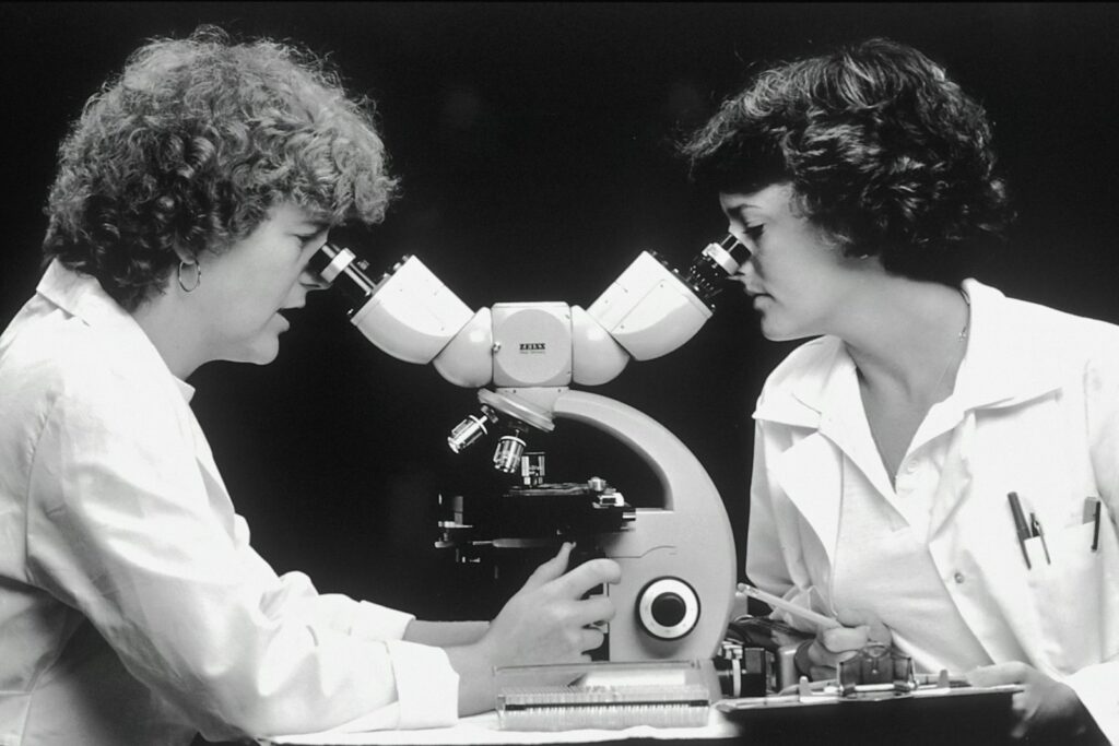 Two Caucasian women scientists looking through a double-headed microscope.